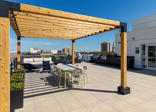 A wooden pergola is over a patio with chairs and tables.