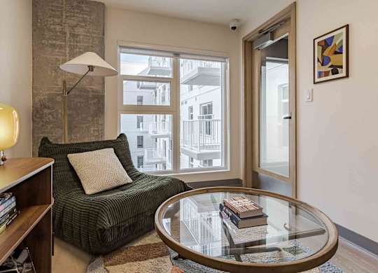 A living room with a green couch, a glass table, and a lamp.