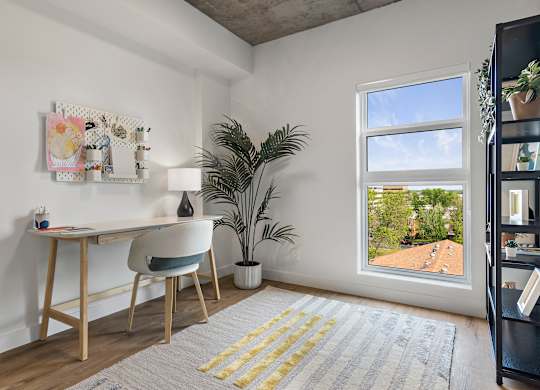 A room with a desk, chair, and a window overlooking a roof.