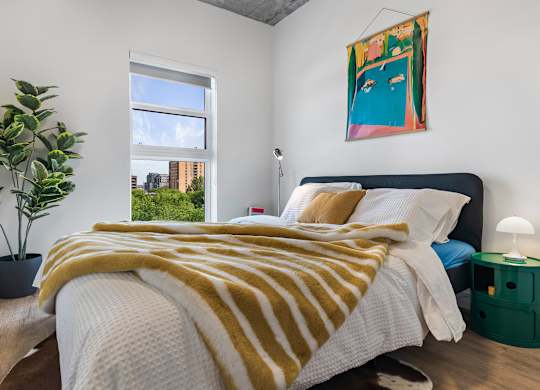 A bedroom with a bed covered in a yellow and white striped blanket.