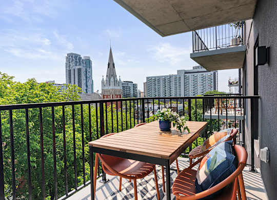 A balcony with a table and chairs overlooking a city skyline.