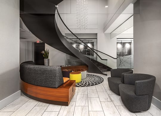 A modern living room with a curved sofa, armchairs, and a staircase at Clayton on the Park Apartments, Missouri, 63105