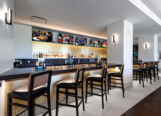 A bar with black chairs and a counter with bottles on it at Clayton on the Park Apartments, Clayton, Missouri