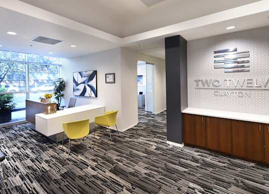A reception area with a desk and chairs in front of a Two Twelve Clayton sign.