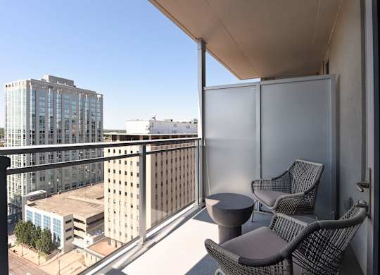 A balcony with two chairs and a table overlooks a cityscape.