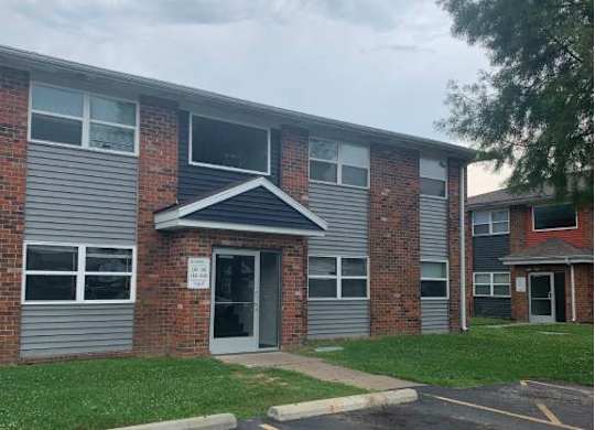 the front of a building with a parking lot and grass