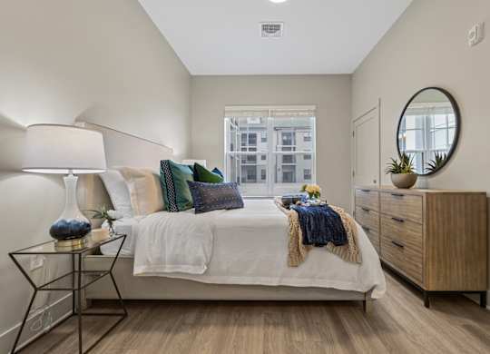 A bedroom with a bed, nightstand, and a window with a view of a city.
