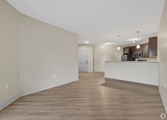 A spacious room with wooden flooring and a kitchen area in the background.