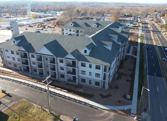 A large white building with a grey roof is surrounded by roads.