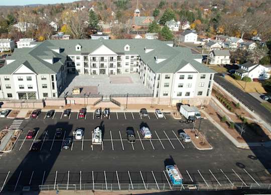 A large white building with a green roof is surrounded by a parking lot.