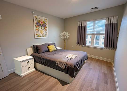A bedroom with a bed, nightstand, and a painting on the wall.