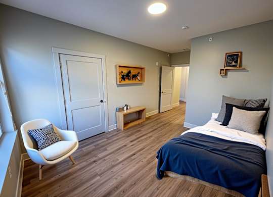 A bedroom with a bed, chair, and artwork.