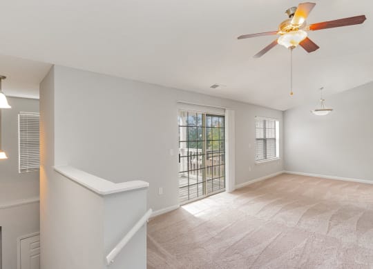 an empty living room with a ceiling fan and a door to a balcony