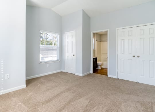 an empty living room with carpet and a door to a bathroom