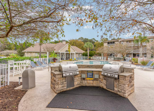 a patio with a grill and a pool with chairs at Litchfield Oaks Apartments, Pawleys Island, SC