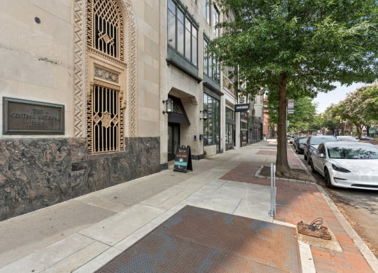 a sidewalk with a tree and cars parked on the side of the road
