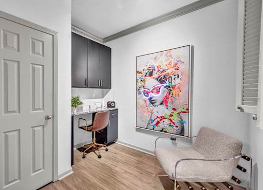 A room with a chair, a desk, and a painting on the wall.