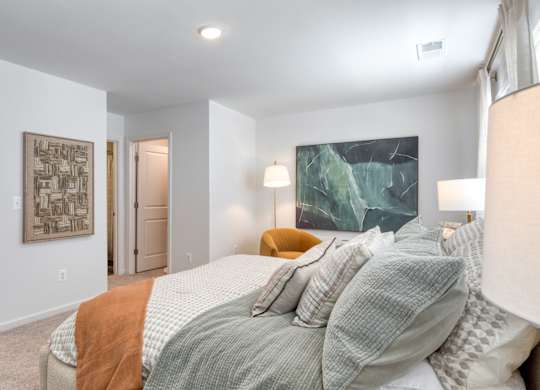 A bedroom with a bed, a lamp, and a painting on the wall at The Mark Townhomes Apartments, Harrisonburg, VA