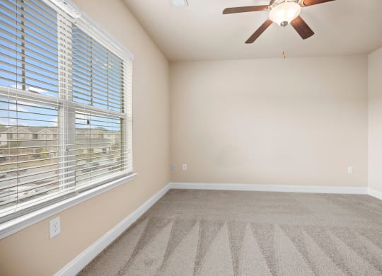 an empty living room with a large window and a ceiling fan