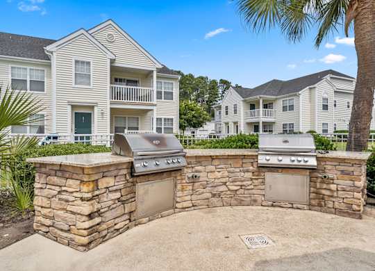 A stone wall with two built-in BBQs in front of a two-story apartment building.