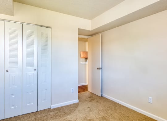 an empty bedroom with white closets and a hallway to a bathroom
