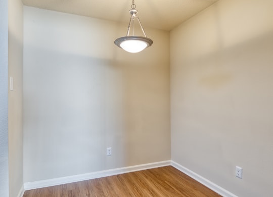 an empty living room with wood flooring and a light hanging from the ceiling
