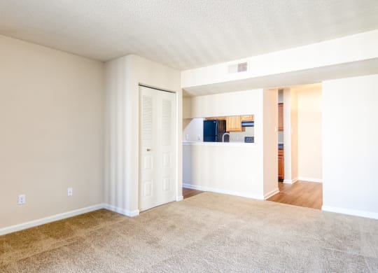 an empty living room with a kitchen in the background