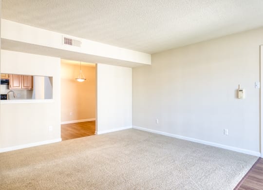an empty living room with a white door and a kitchen