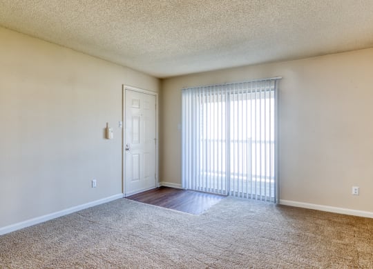the spacious living room of an apartment with a large window and a door