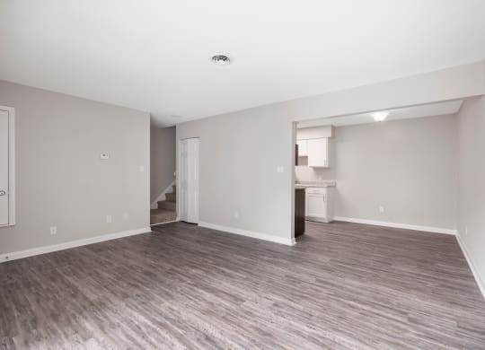 an empty living room with a kitchen in the background