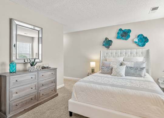 A bedroom with a large bed, a dresser, and a mirror.