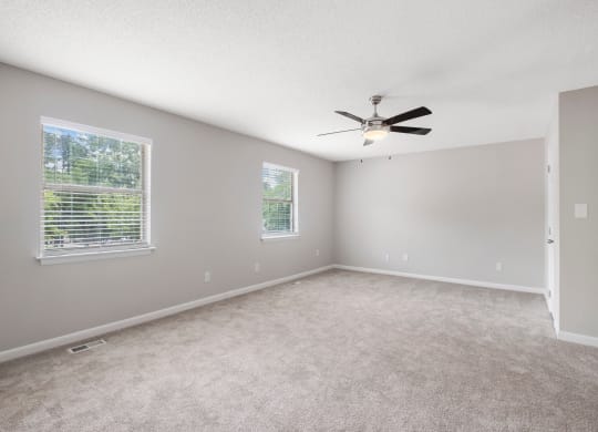 an empty bedroom with a ceiling fan and three windows