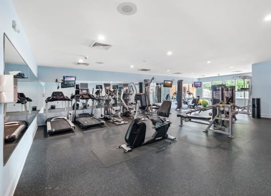 a spacious fitness room with cardio equipment and flat screen tvs
