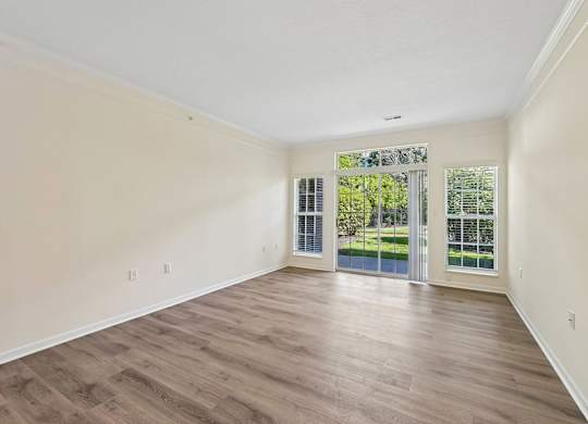 A room with wooden flooring and a sliding glass door leading to a backyard.