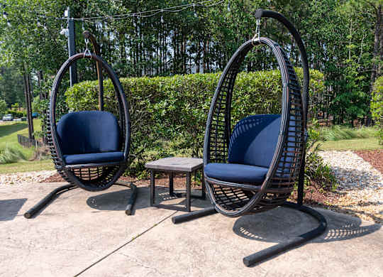 Two hanging chairs with blue cushions are placed in a garden.