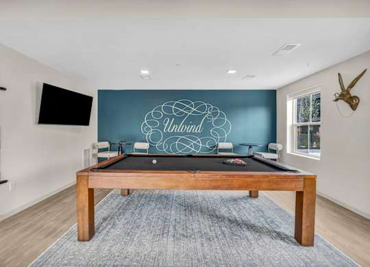 A pool table with a blue cloth and a wooden frame is in the middle of the room.