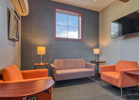 A living room with a grey carpet and a grey wall with a window and a flat screen TV.
