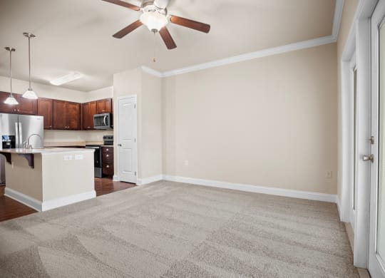 an empty living room with a ceiling fan and a kitchen