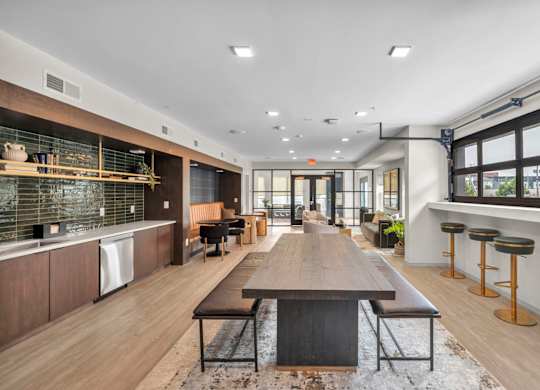 A modern kitchen with a long wooden table in the middle.