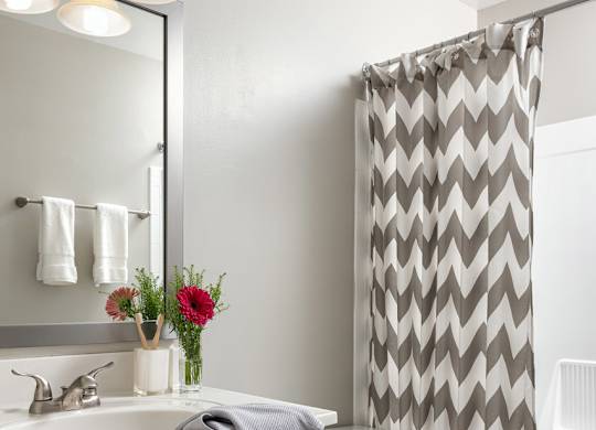 A bathroom with a white toilet, sink, and a grey and white shower curtain.