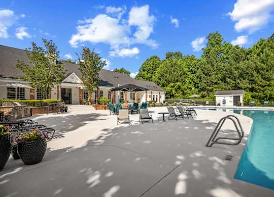 A pool area with a swimming pool, lounge chairs, and a building in the background.