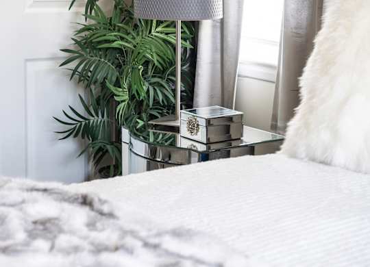 A bed with a white comforter and a small box on a glass table.