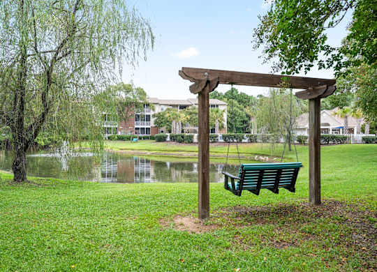 A wooden swing set sits in a grassy area next to a pond at Litchfield Oaks Apartments in Pawleys Island, SC
