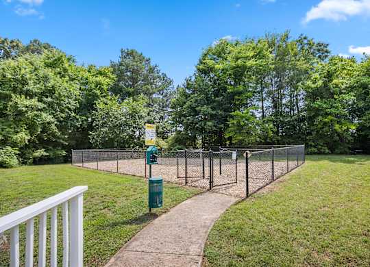 A green trash can sits on a concrete path next to a chain link fence.
