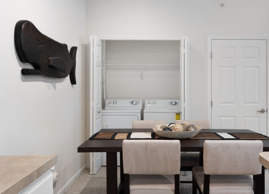 a dining room with a wooden table and chairs and a white kitchen with a sink at The Charleston, Columbus, OH, 43221