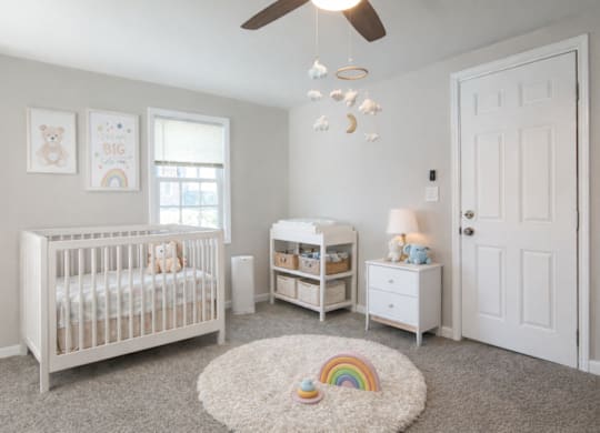 A baby nursery with a white crib, changing table, and a rainbow rug.
