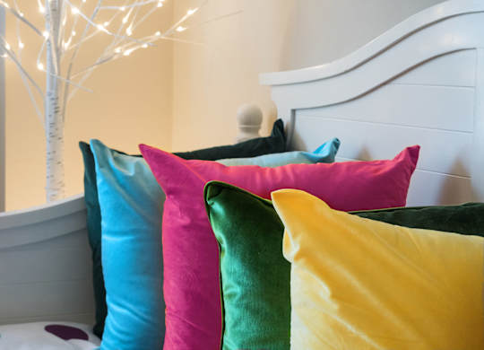 A white bed with colorful pillows in front of a white tree.