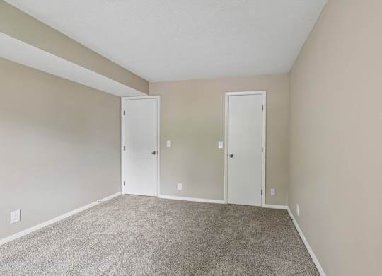 A room with carpeted floor and three white doors.