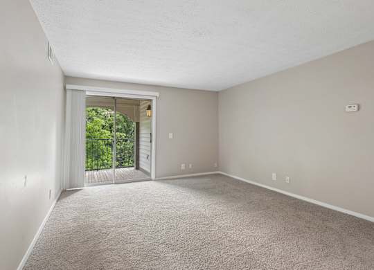 A room with a carpeted floor and a sliding glass door leading to a balcony.
