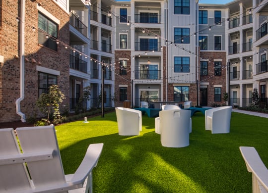 an outdoor lounge area with chairs and grass in front of an apartment building